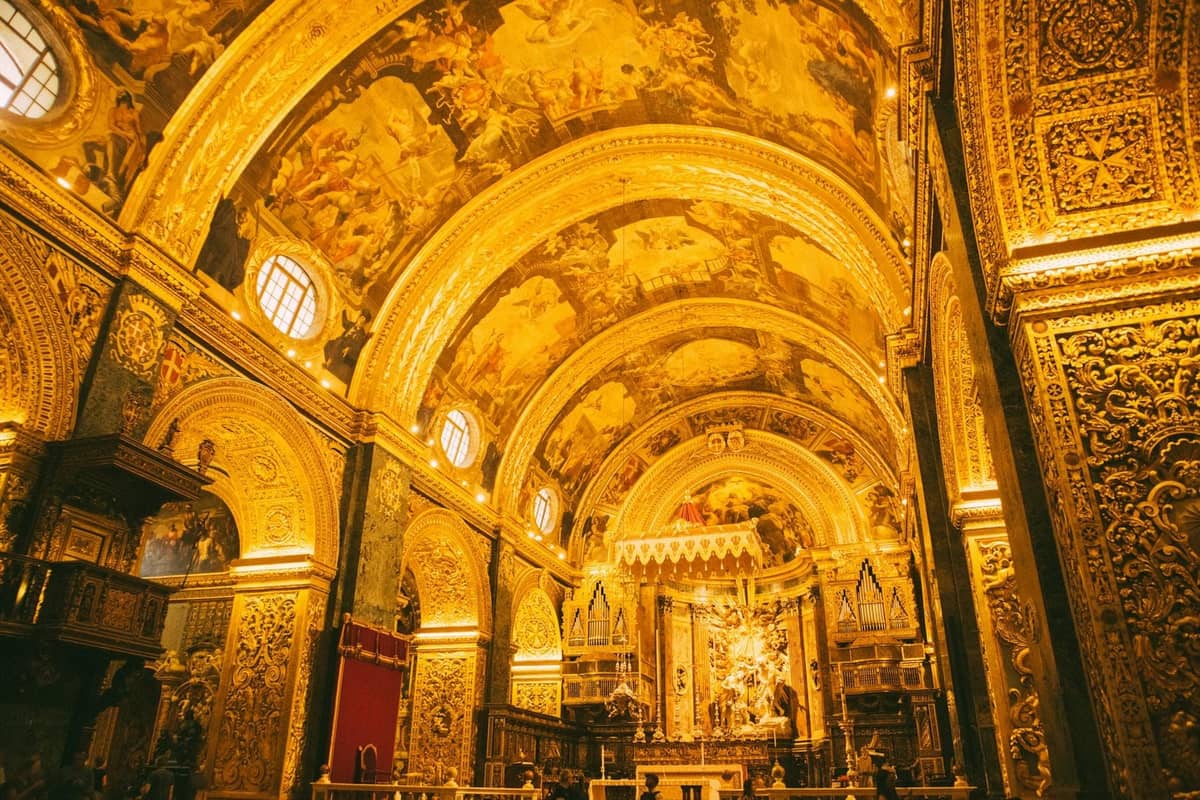 Złote, bogato zdobione barokowe wnętrze katedry z łukowymi sufitami, ozdobnymi rzeźbieniami i dziełami sztuki religijnej nad ołtarzem.