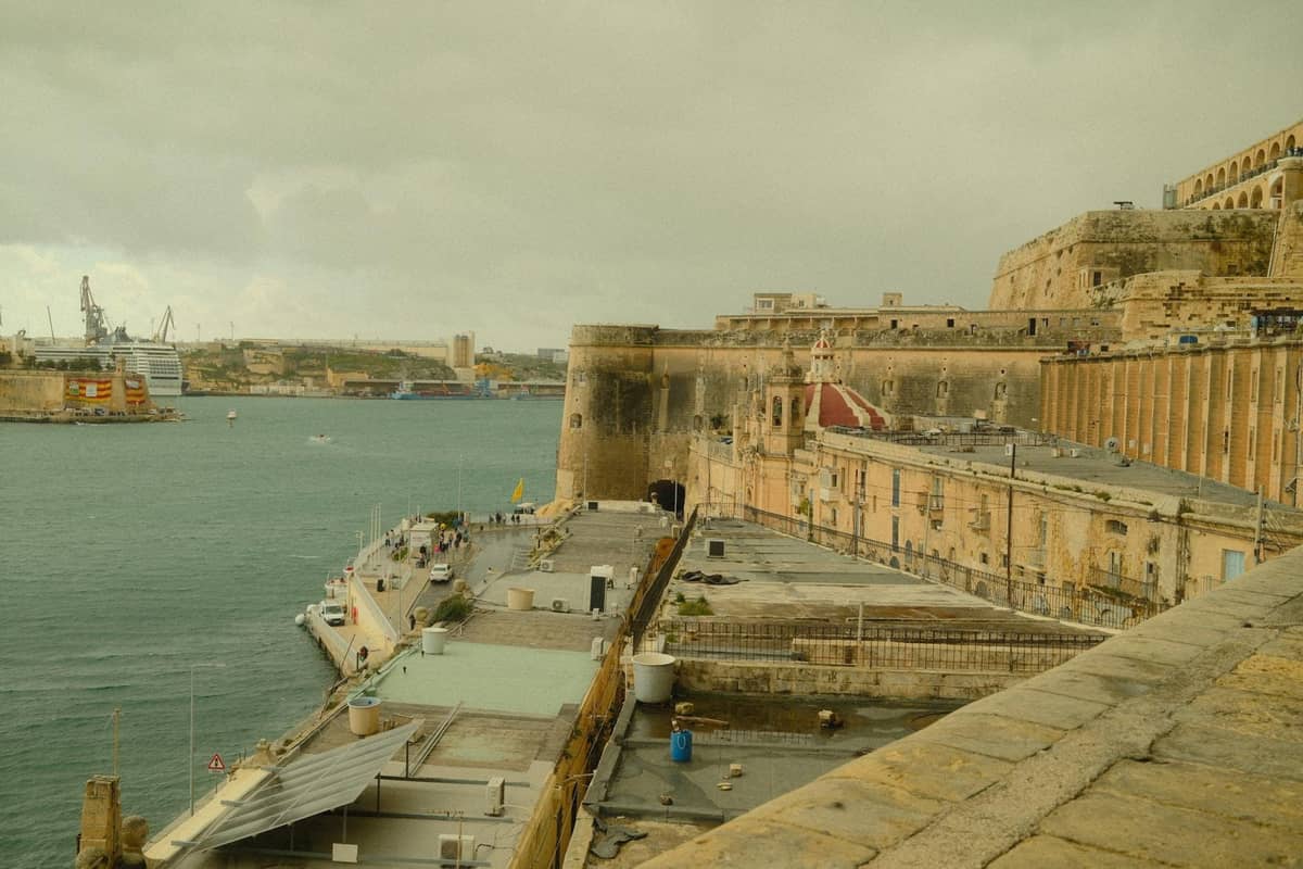 Widok dużej kamiennej fortyfikacji nad wodą w Valletcie, Malta, z historycznymi murami i budynkami z widokiem na port.