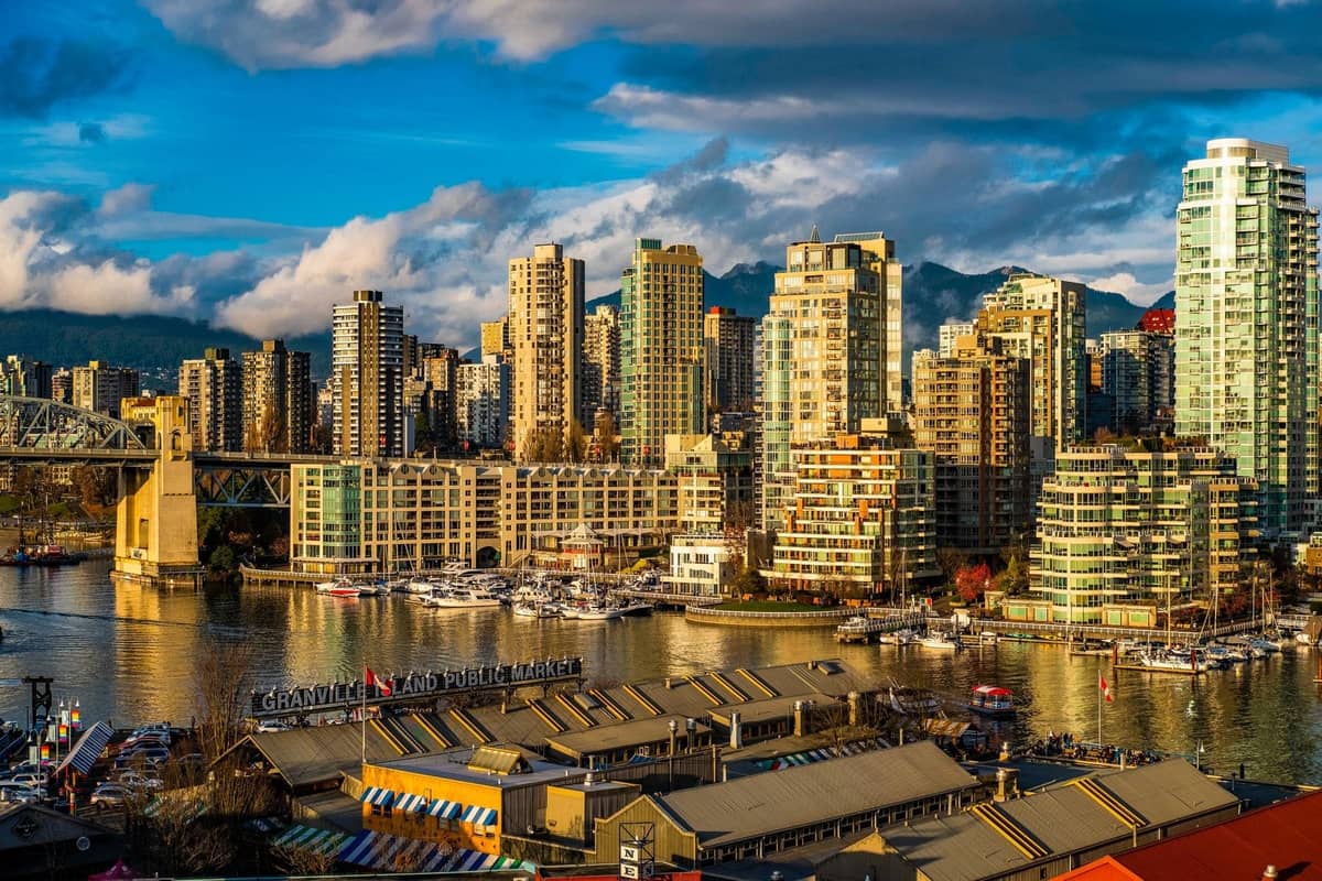 Bunte öffentliche Marktgebäude im Vordergrund mit Blick auf False Creek mit Booten, Hochhäusern und der Burrard Bridge in Vancouver, BC.