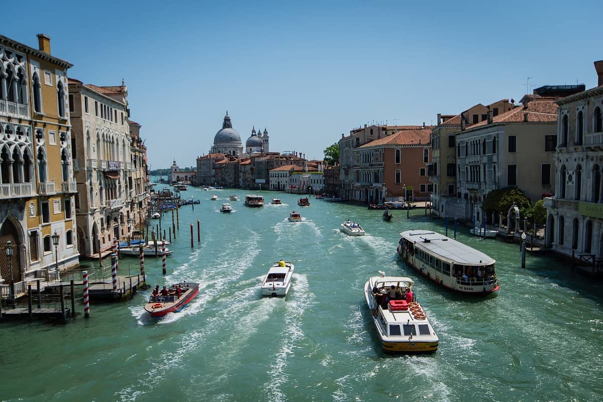 Weitläufige Aussicht auf den Canal Grande in Venedig mit Booten, Wassertaxis und historischen Palazzi auf beiden Seiten unter einem klaren blauen Himmel.
