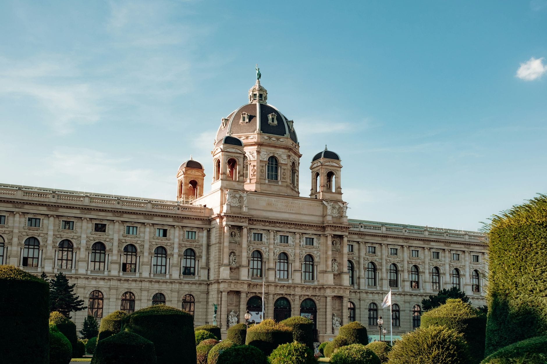 Weitblick auf das Kunsthistorische Museum in Wien unter klarem blauen Himmel, flankiert von gepflegten Gärten und Bäumen.