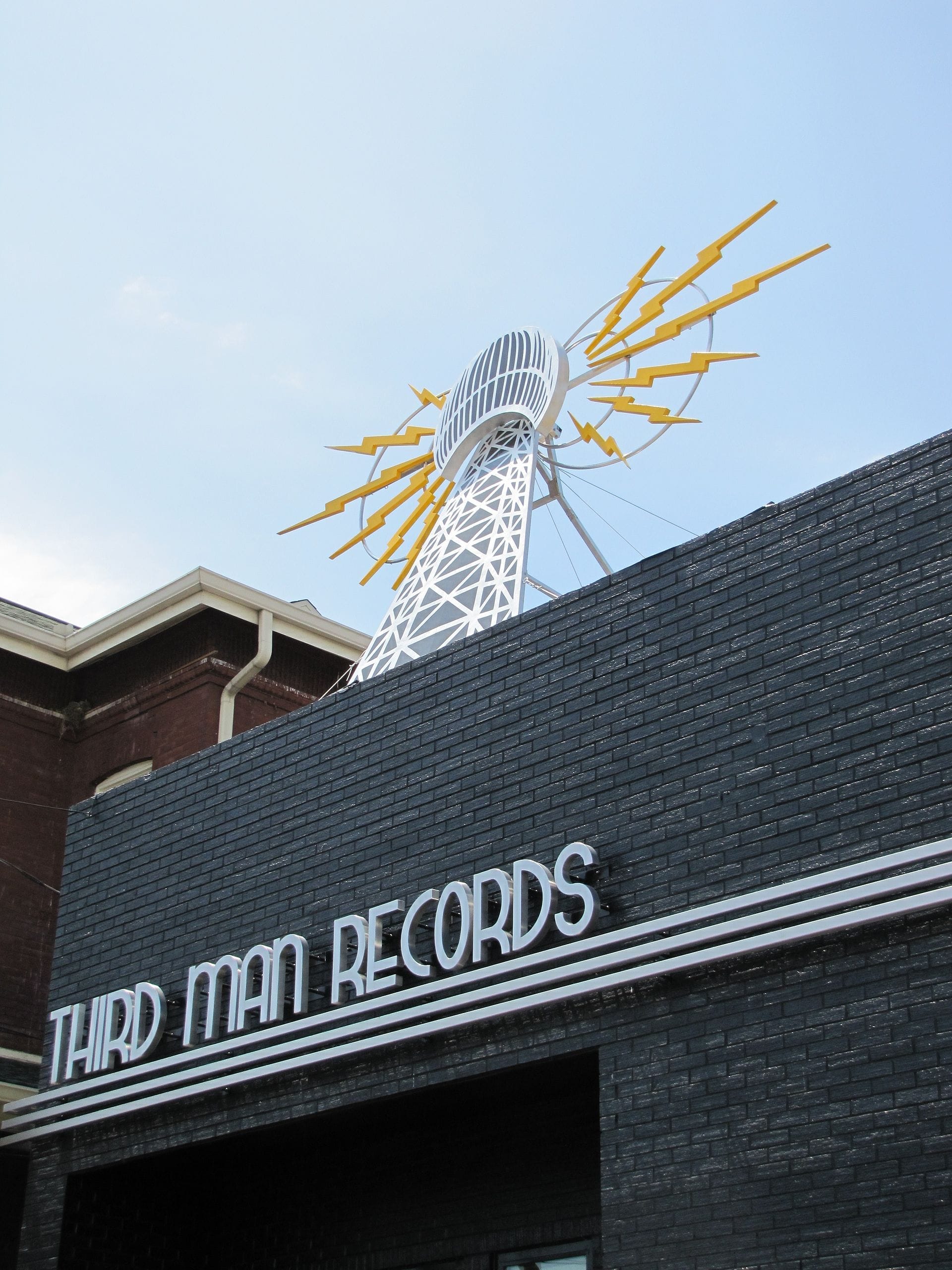 El exterior de Third Man Records en Nashville, con una fachada de ladrillo negro y una llamativa escultura con rayos amarillos contra un cielo azul.