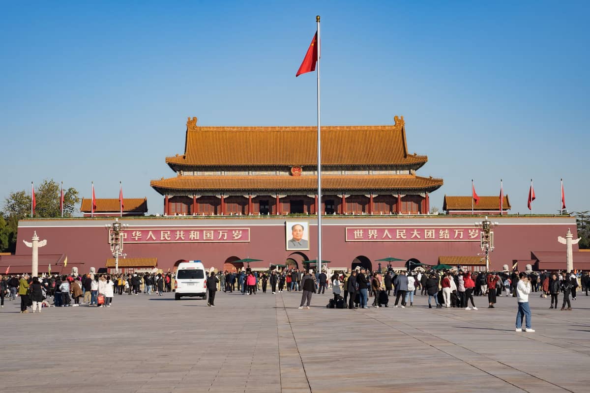 Weiter Blick über den Platz des Himmlischen Friedens mit Menschenmassen, zentralem Fahnenmast und dem ikonischen Tor des Himmlischen Friedens unter einem klaren blauen Himmel in Peking.