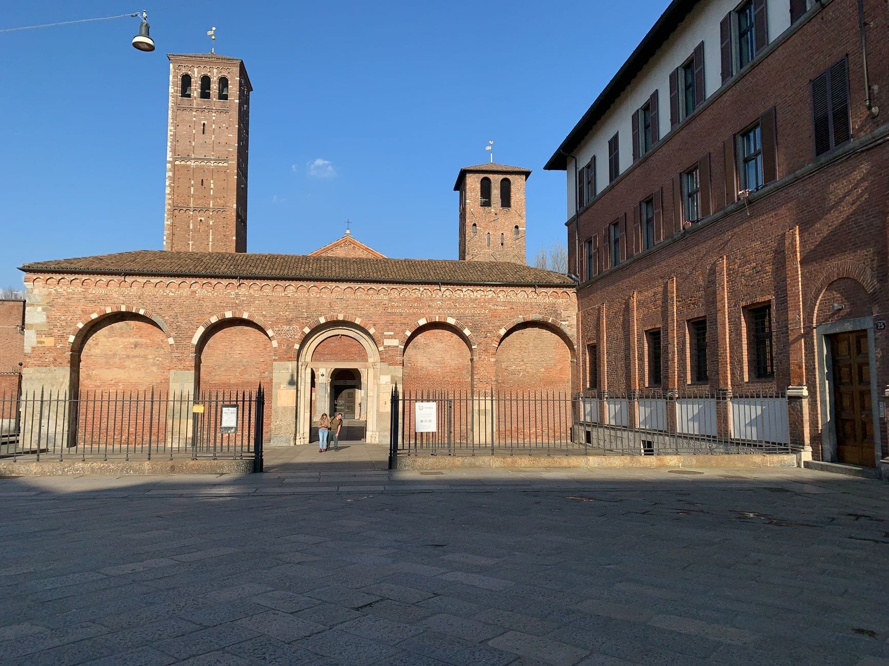 มหาวิหาร Basilica di Sant'Ambrogio ในเมืองมิลาน พร้อมด้วยด้านหน้าอิฐสไตล์โรมาเนสก์ ระเบียงโค้ง และหอระฆังคู่ใต้ท้องฟ้าสีครามใส