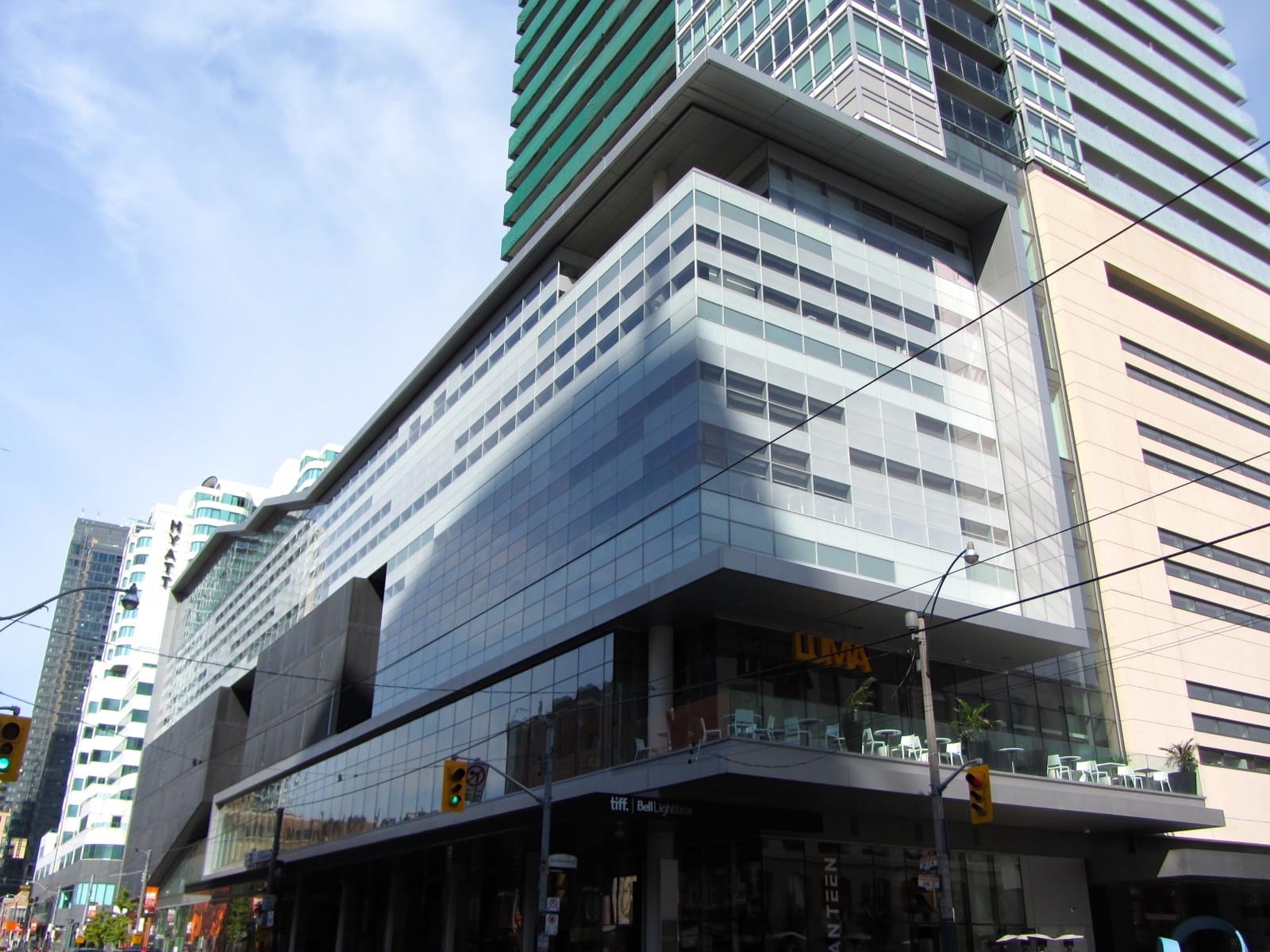 มุมมองภายนอกของ TIFF Lightbox ในเมืองโตรอนโต โดดเด่นด้วยสถาปัตยกรรมกระจกสมัยใหม่และสายไฟรถรางใต้ท้องฟ้าสีฟ้าสดใส