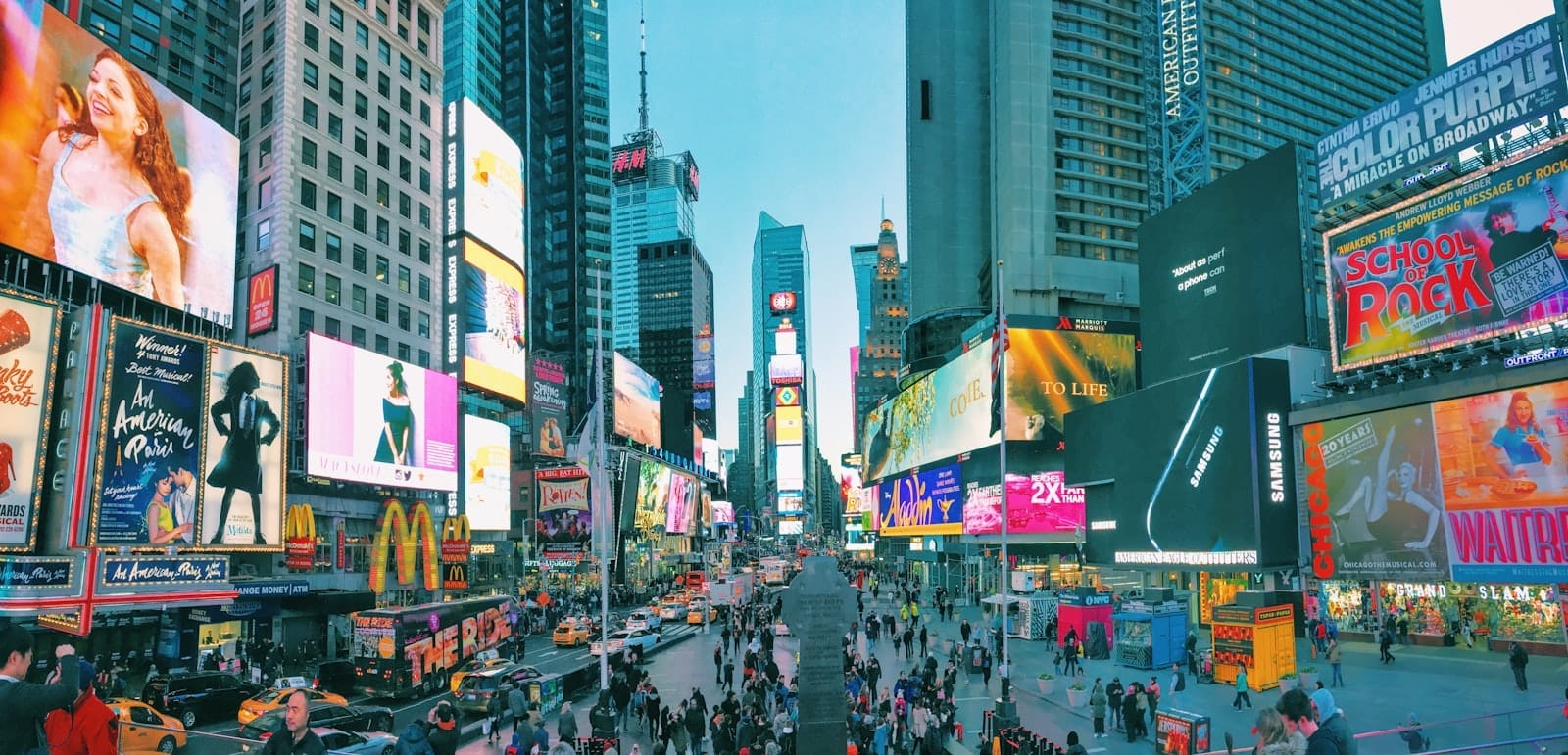 Vista ampia e vibrante di Times Square con folla di persone, taxi e imponenti schermi digitali all'incrocio tra Broadway e la Seventh Avenue, Midtown Manhattan.