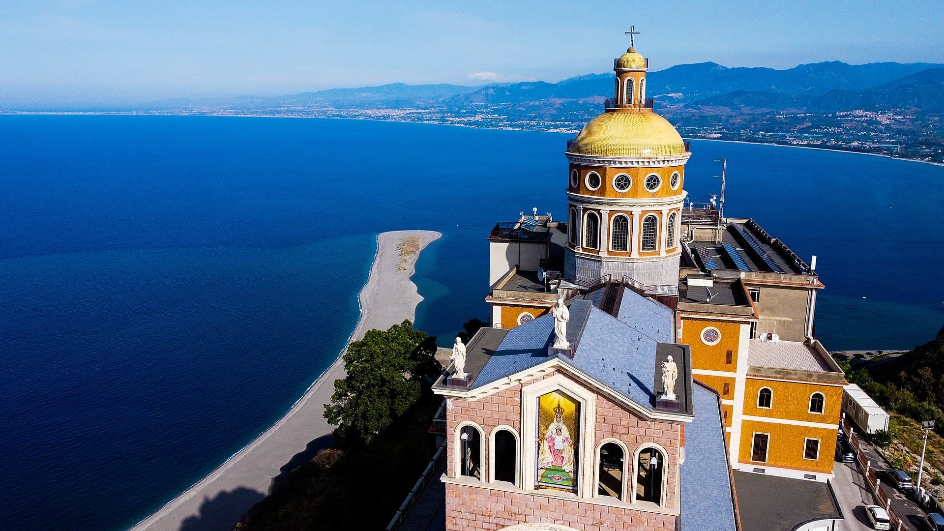 Luftaufnahme des Heiligtums von Tindari mit seiner goldenen Kuppel, mit Blick auf das strahlend blaue Tyrrhenische Meer und die beeindruckende sizilianische Küste.