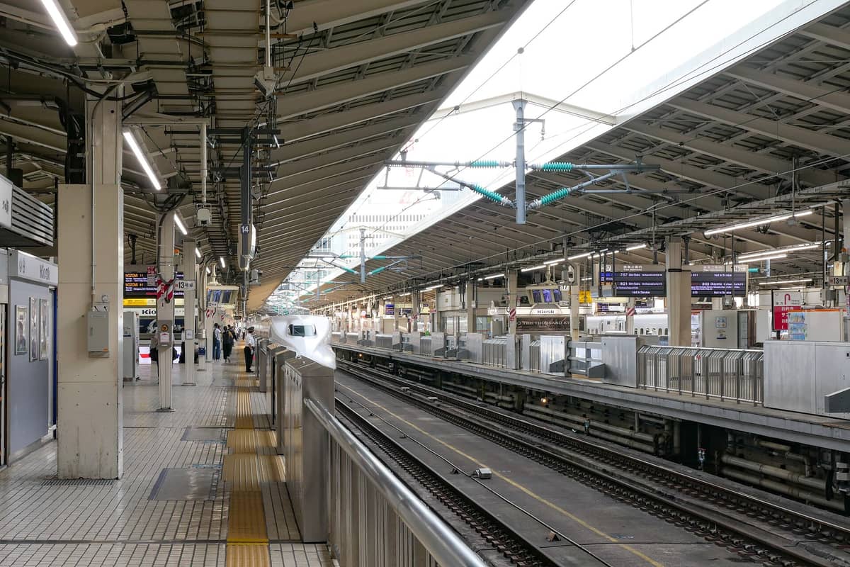 Wide view of Tokyo Station Shinkansen platforms with a bullet train, overhead signs, and passengers waiting.