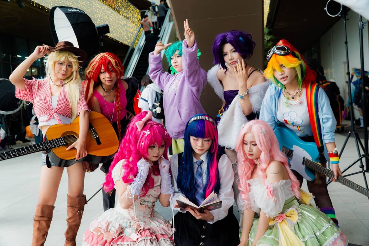 Group of people in colorful anime cosplay costumes posing together indoors at what appears to be a convention or anime event.