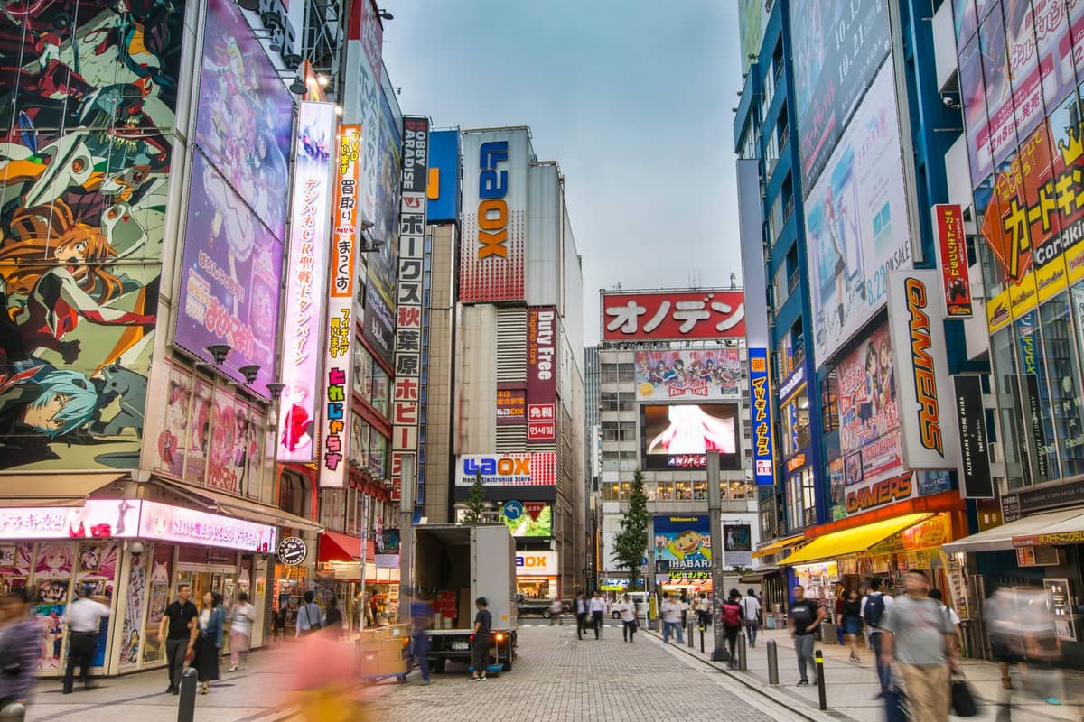 Street view of Akihabara in Tokyo with colorful anime and manga billboards, shops, and crowds of people in the famous otaku shopping district during daylight.