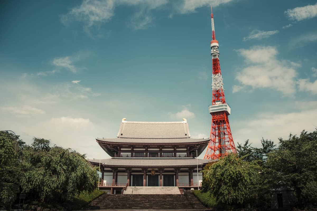 A traditional Buddhist temple with Tokyo Tower rising directly behind it, capturing both historic and modern architecture in one frame.