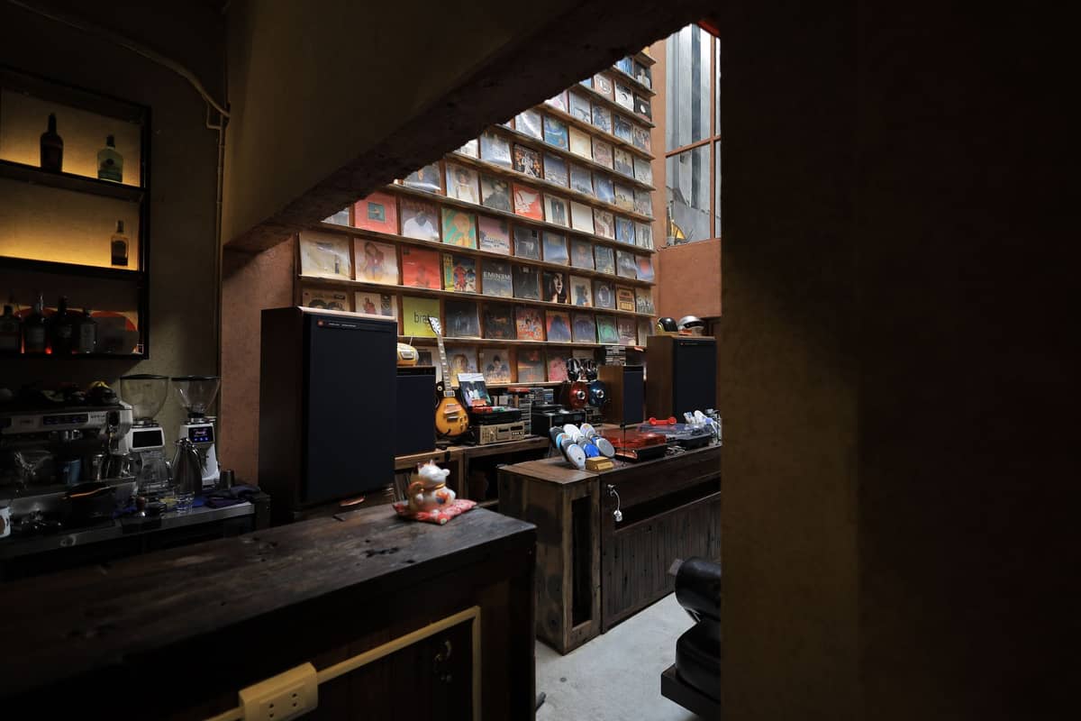 Dimly lit interior of a retro Japanese café with vinyl records on shelves, wooden bar counter, and classic audio equipment.