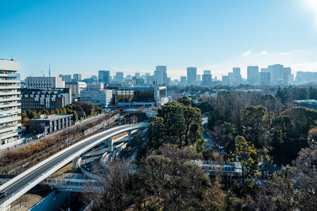 Daytime Tokyo cityscape with highways, greenery, and distant skyline under clear blue sky, emphasizing urban transit and connectivity.