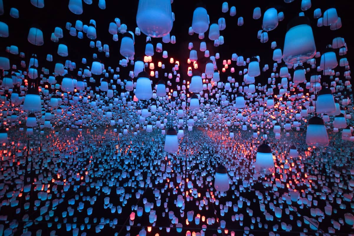 Immersive digital art installation with hundreds of glowing blue and pink lanterns suspended in a mirrored room at teamLab Borderless in Tokyo.