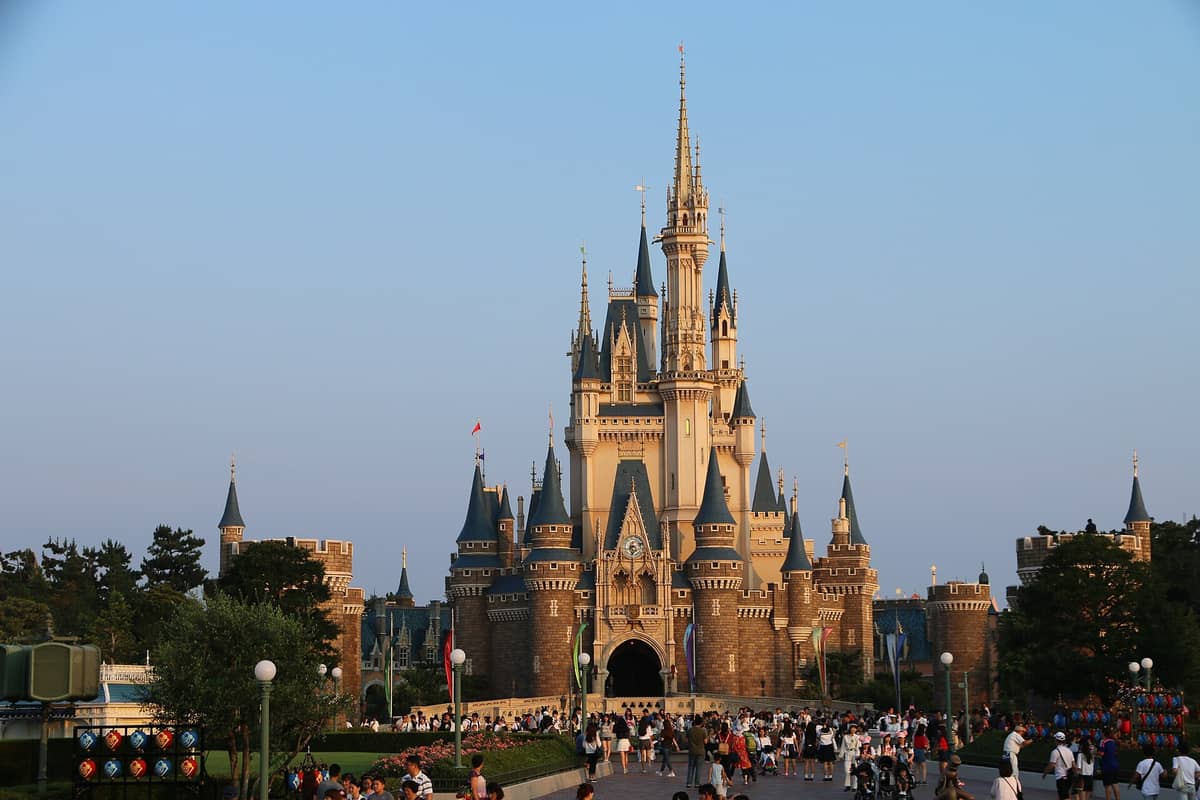 Wide view of Tokyo Disneyland’s iconic Cinderella Castle with crowds of visitors in front, clear blue sky overhead, and park atmosphere in the afternoon light.