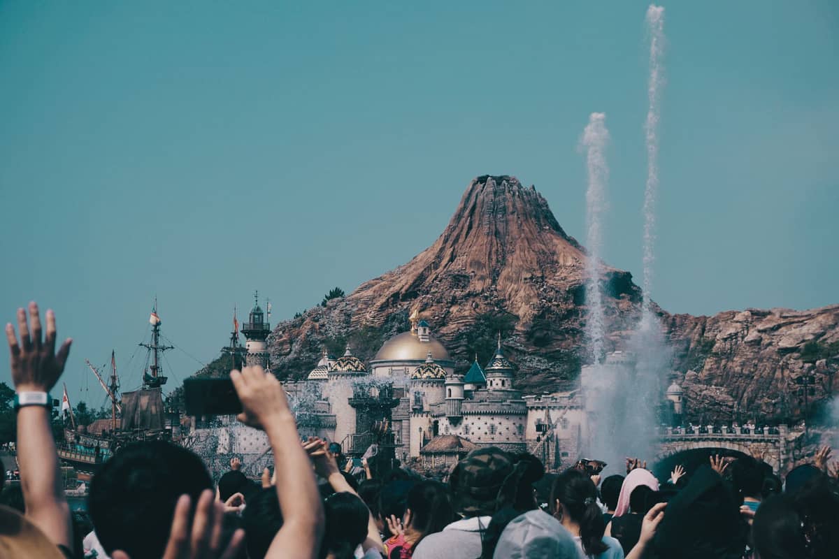 Crowds watch a water and fountain show in front of Mount Prometheus and Mediterranean Harbor at Tokyo DisneySea on a sunny day.