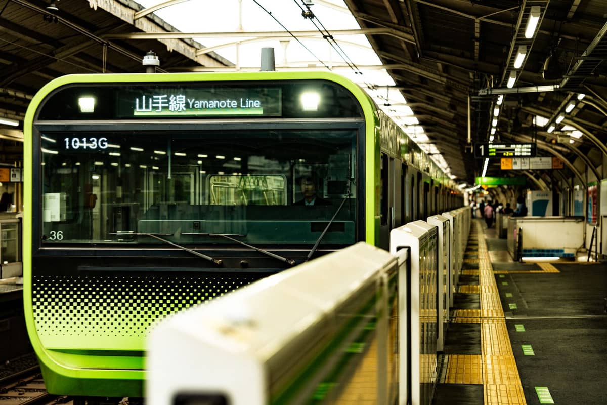 Tokyo’s Yamanote Line train at a station platform, shot head-on, with Japanese and English signage and yellow tactile lines visible.