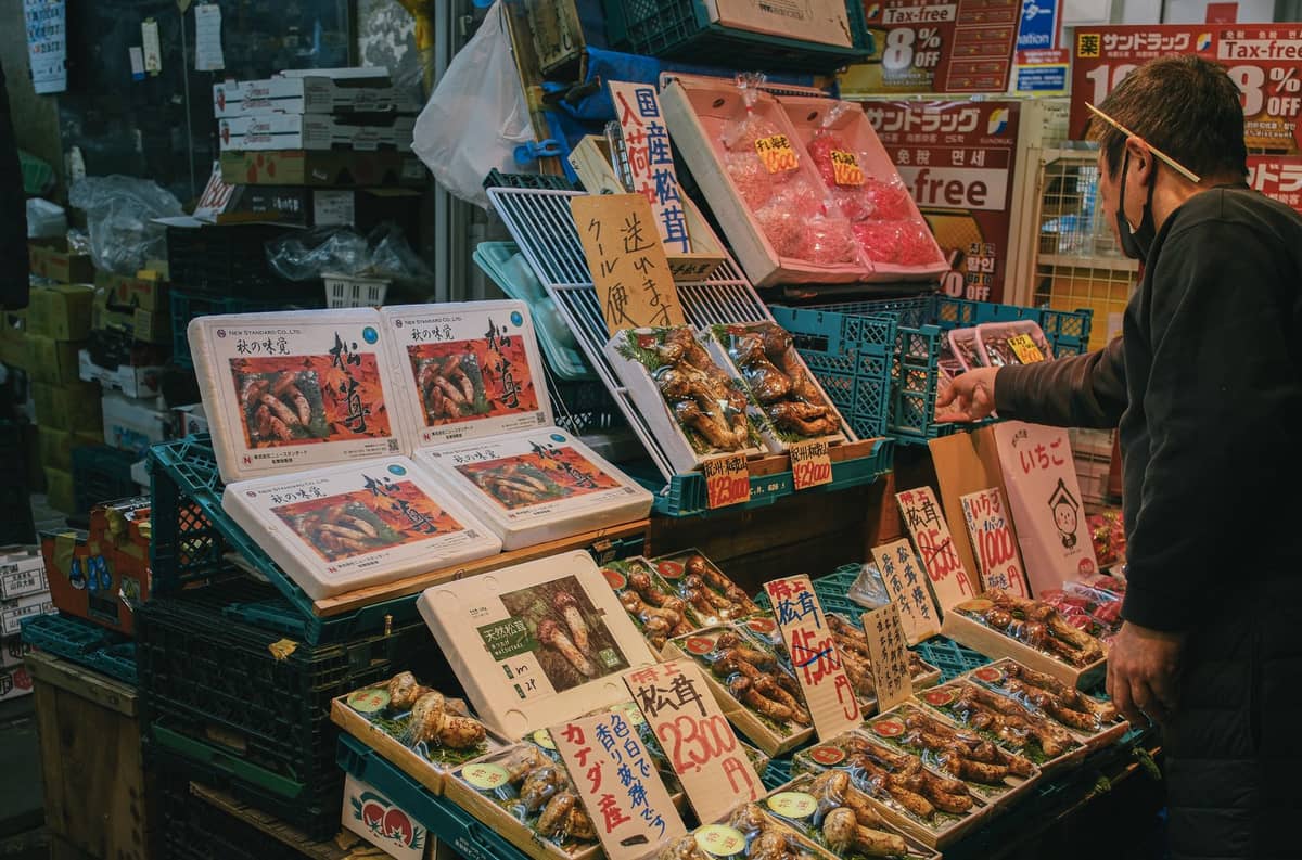 Seafood stall in a Japanese market with trays of fresh fish and handwritten price signs, a man browsing the selection.