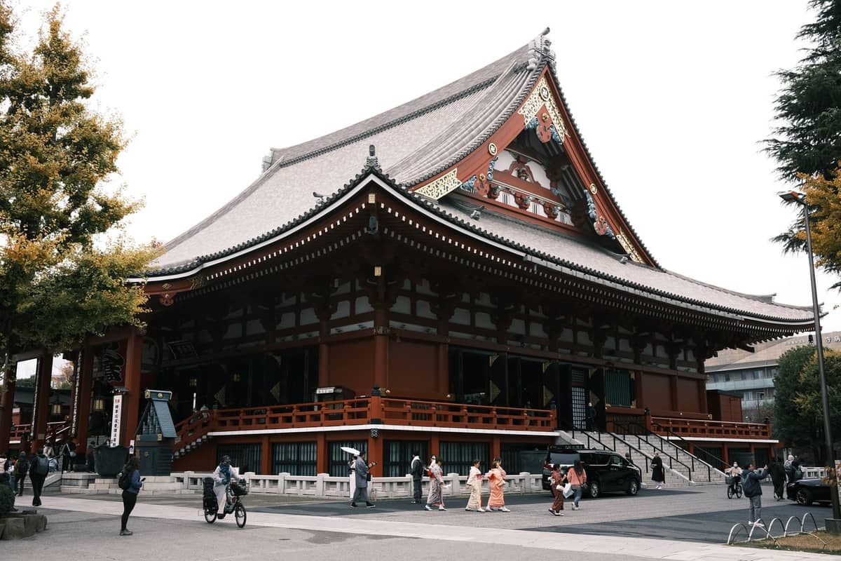 Wide view of Tokyo’s Senso-ji Temple with visitors walking outside, autumn trees, and traditional architecture in daylight.