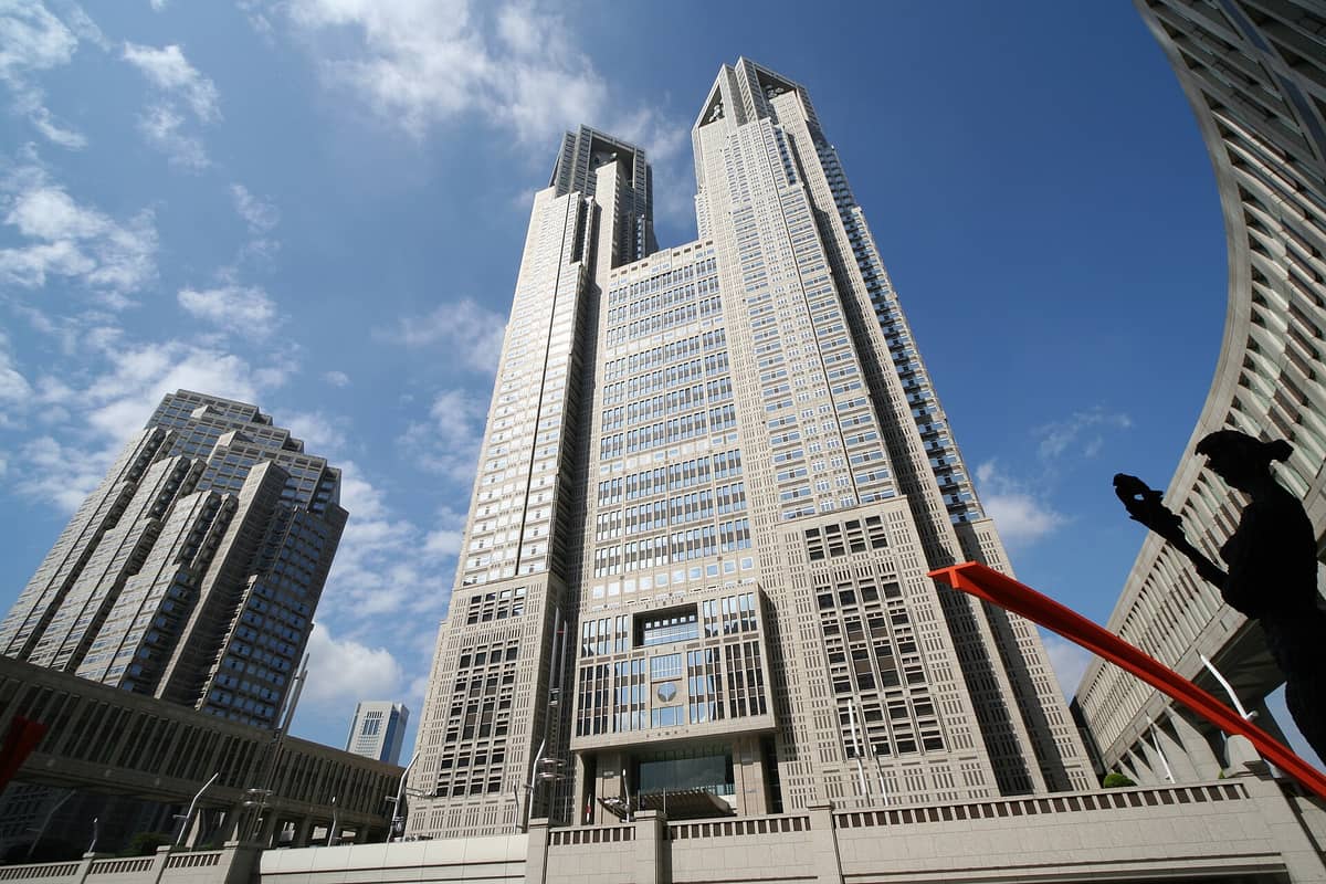 Wide-angle view of the Tokyo Metropolitan Government Building’s iconic twin towers on a sunny day, with a blue sky and surrounding modern buildings in Shinjuku.