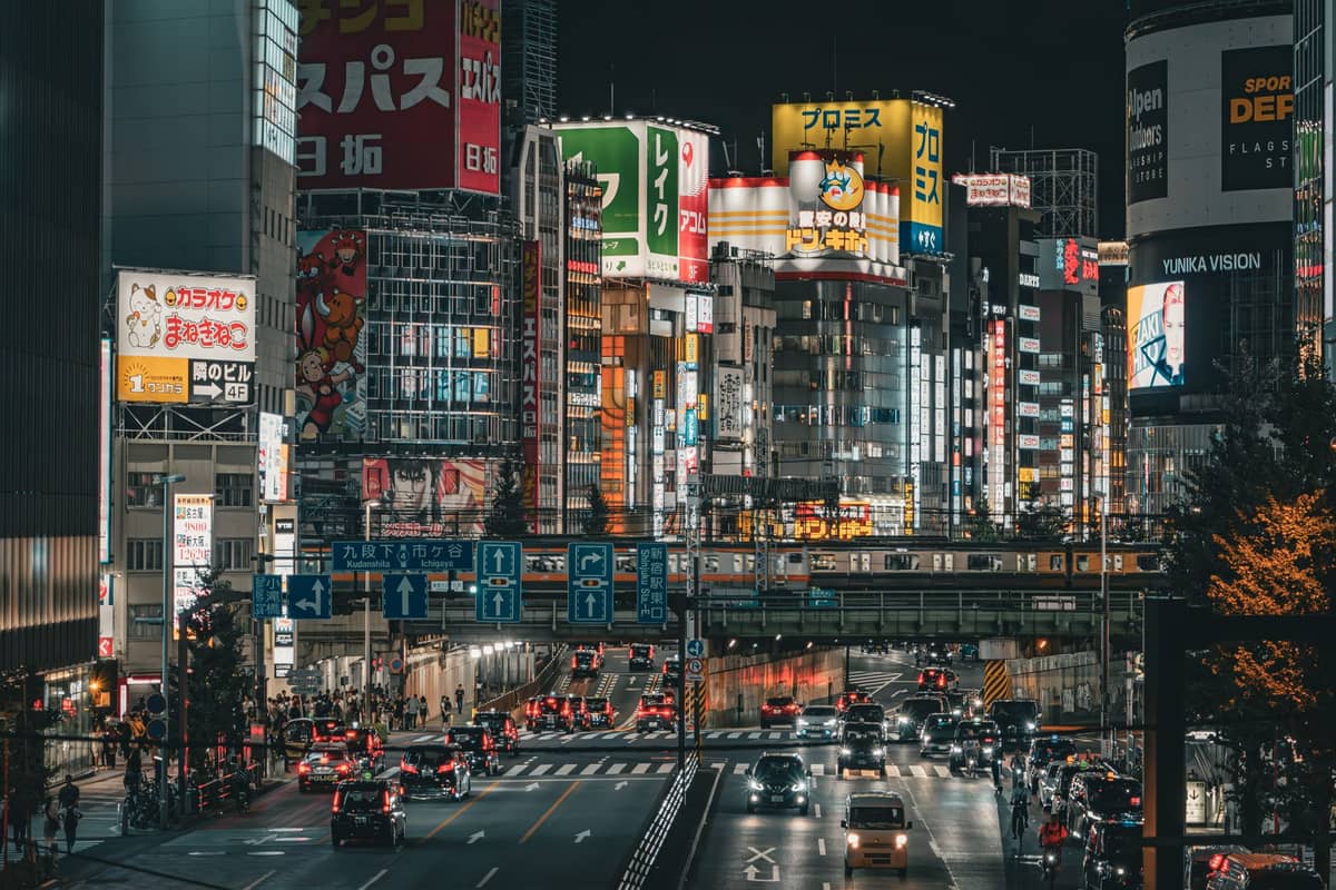 Bustling night street in central Tokyo with dense traffic and tall colorful neon-lit buildings.