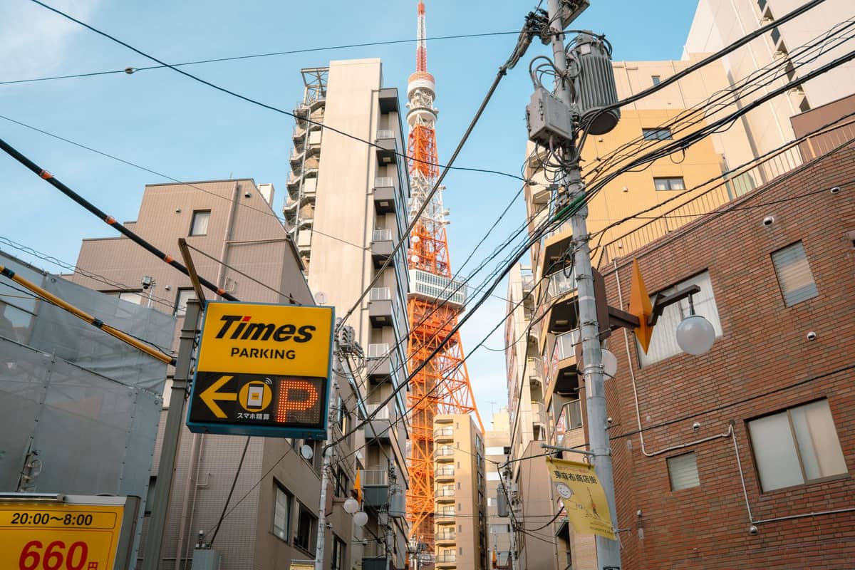 Tokyo Tower rising between mid-rise apartment buildings and dense utility wires in a typical Tokyo neighborhood street scene.