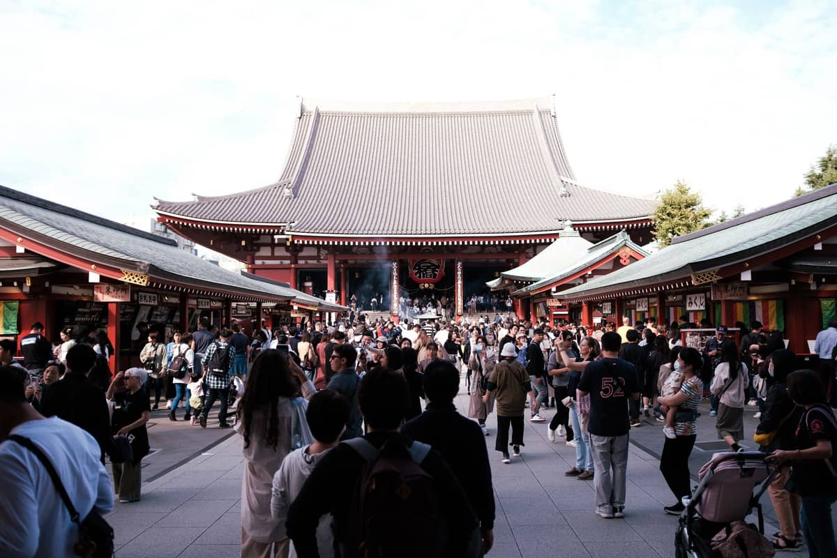 Crowds of people visit Senso-ji, Tokyo’s oldest and most famous temple, with historic buildings and a bustling market street in the foreground.