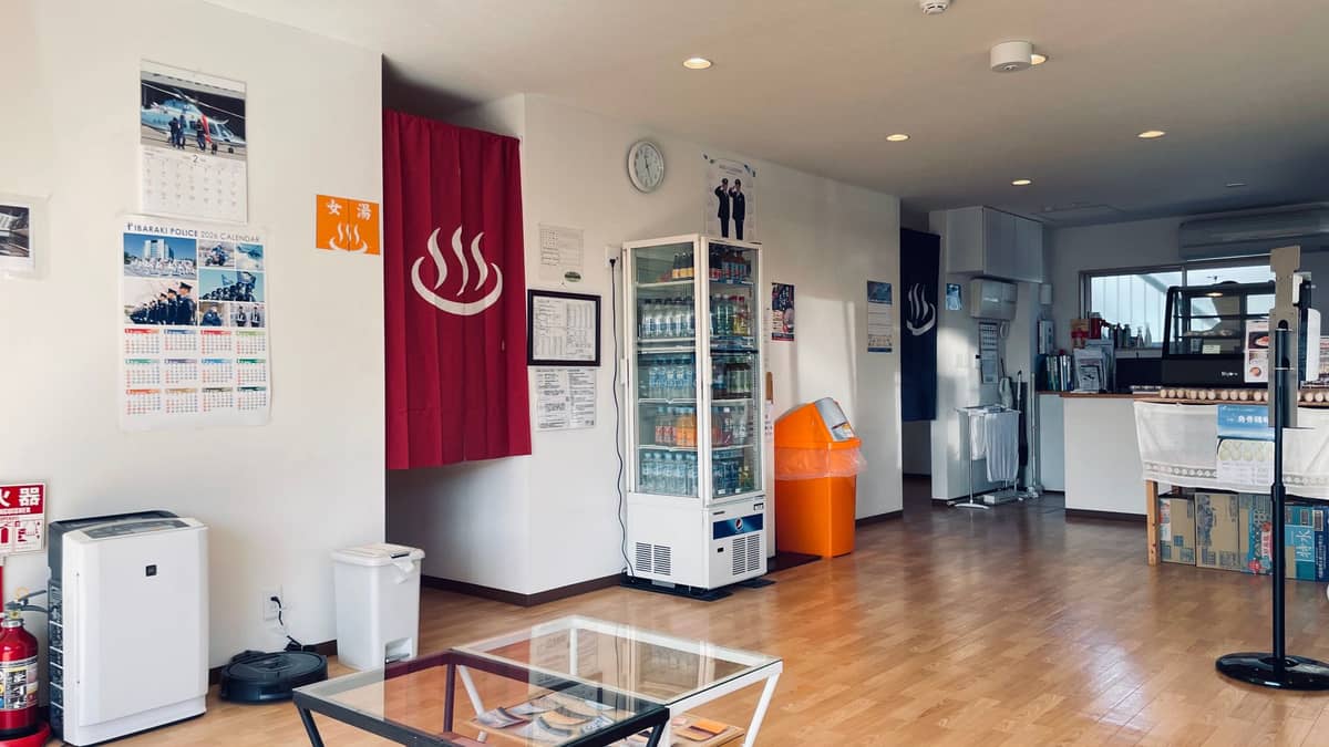 Interior of a Japanese onsen or sento with vending machines, wooden floor, noren curtain, and relaxation area in Tokyo.