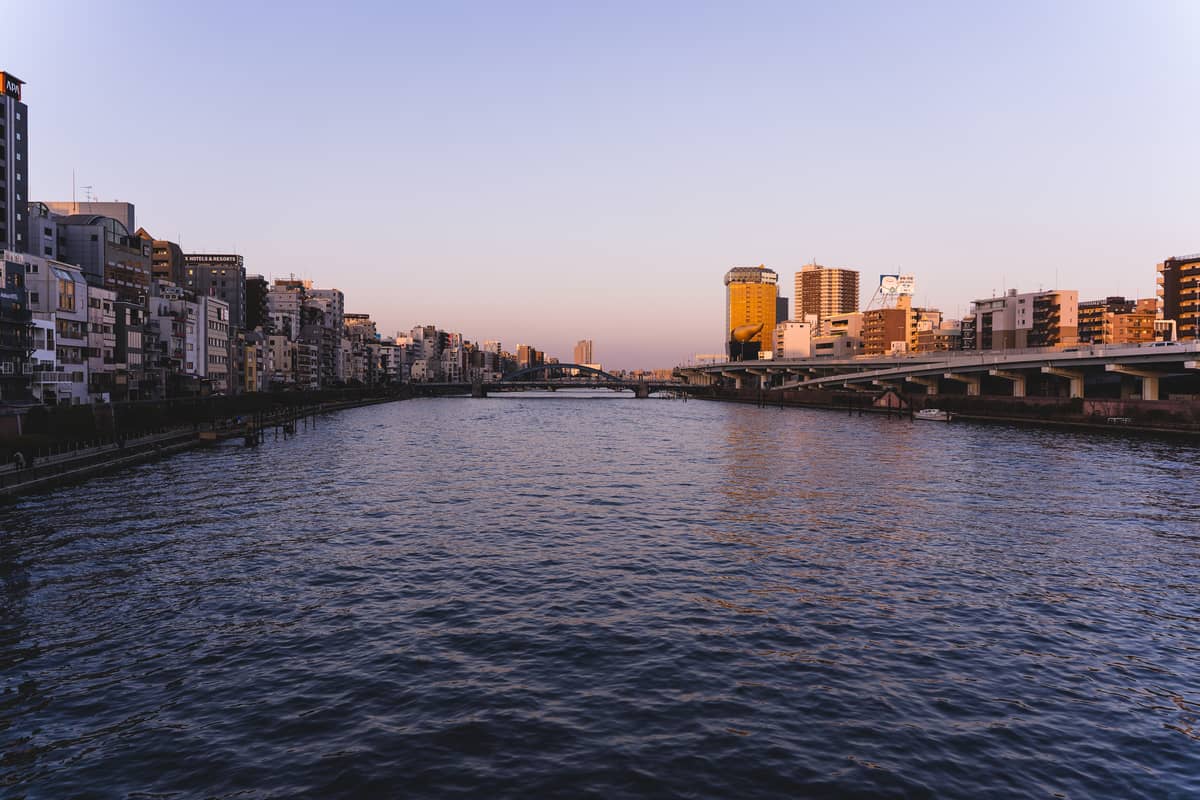 Wide view of the Sumida River at sunset with bridges and Tokyo city buildings, ideal for fireworks viewing spots.