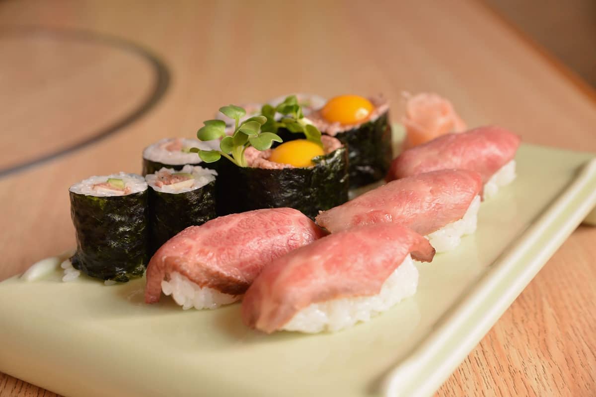 Plate of otoro and chutoro nigiri sushi with maki rolls featuring egg yolk, served on a light ceramic plate in a sushi restaurant.