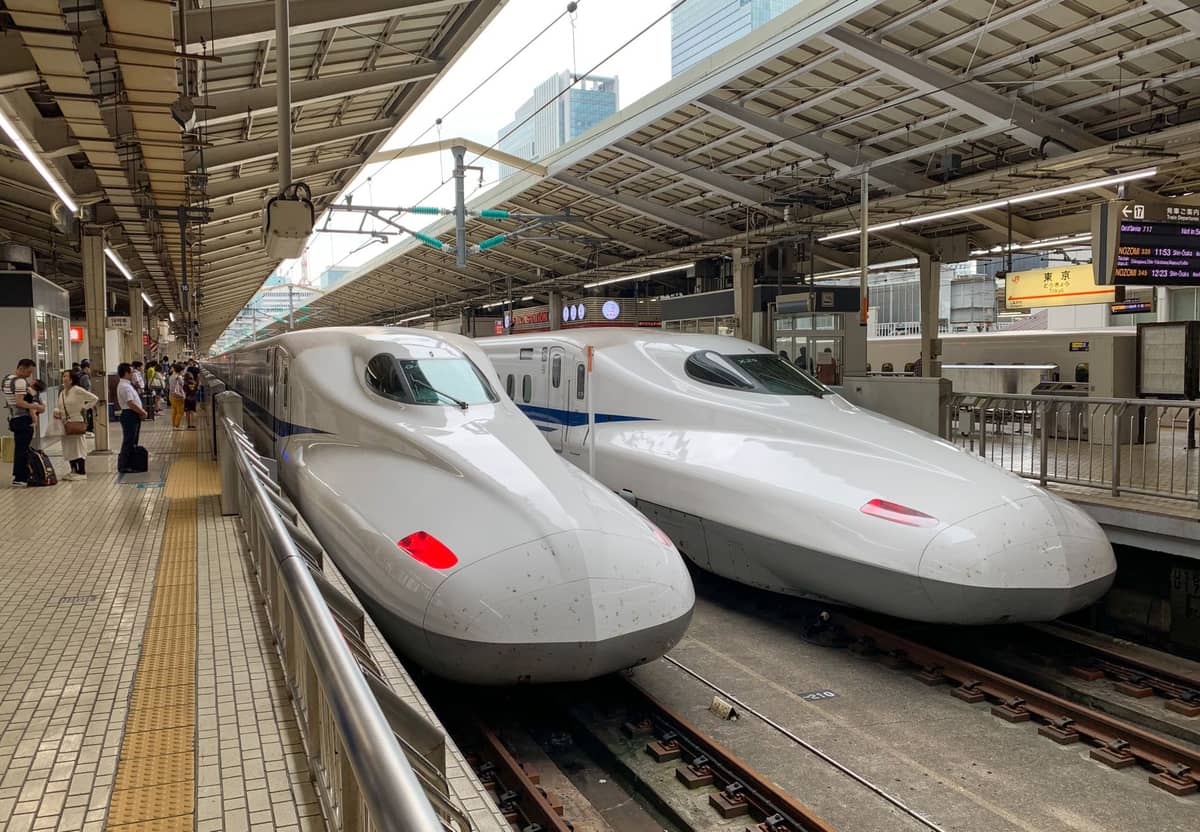 Two N700 Shinkansen bullet trains at a station platform in Japan, clear view of trains and setting under bright daylight.