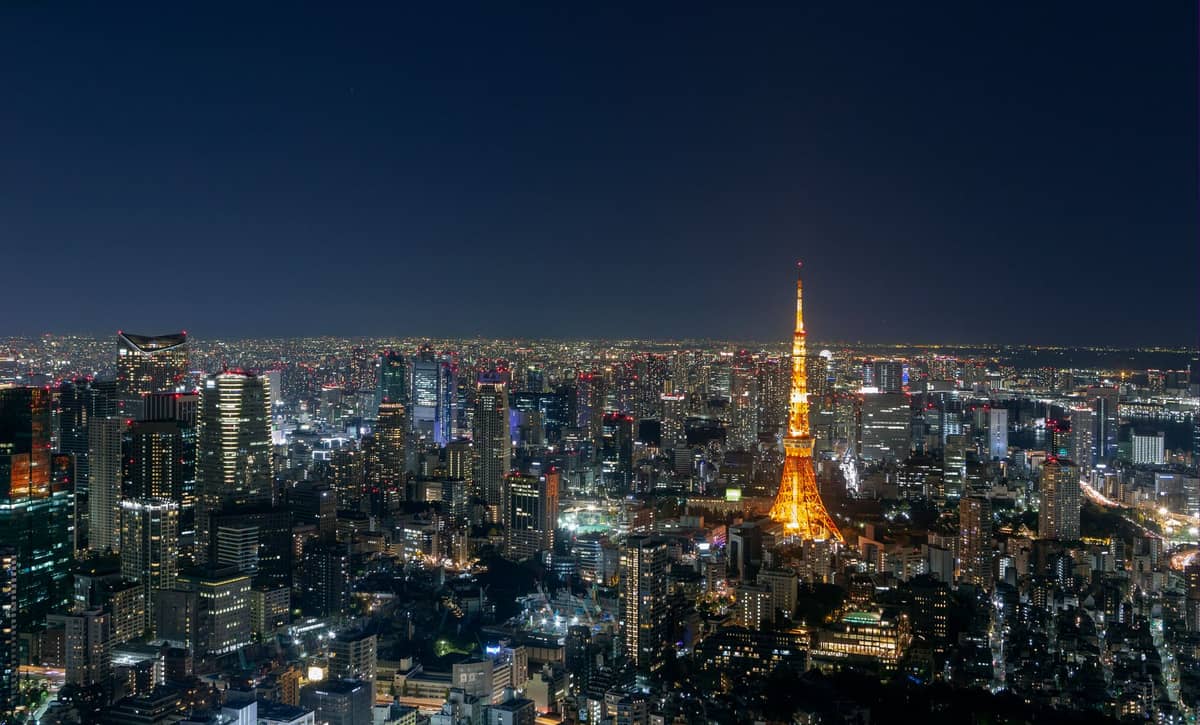 Tokyo skyline at night with Tokyo Tower brightly illuminated in the center surrounded by city buildings and sprawling city lights.