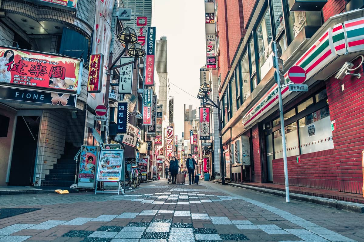 A vibrant Tokyo street scene in a popular neighborhood, with people walking among shops and restaurants lined with colorful neon signs and billboards.