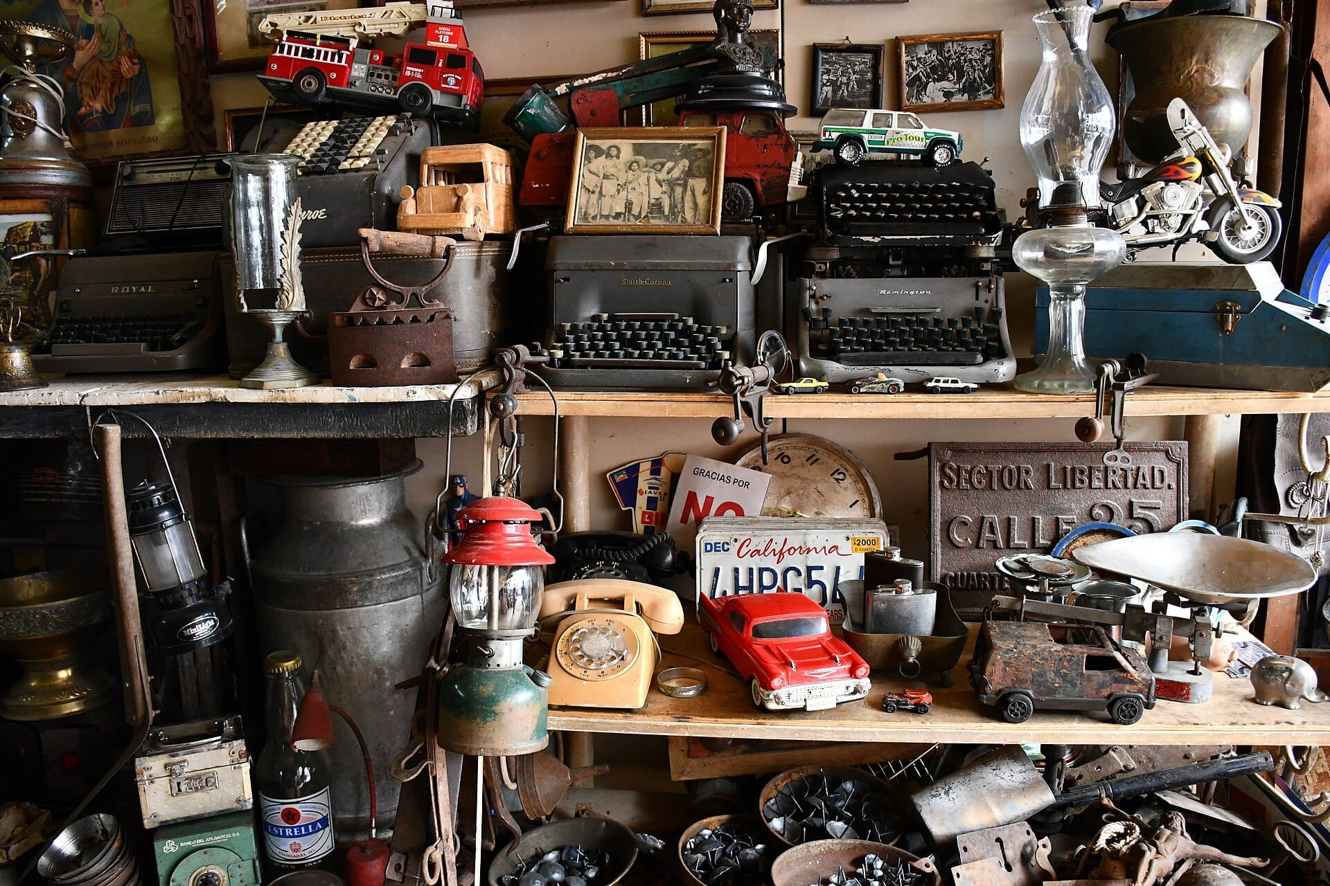 Assortimento di oggetti vintage in esposizione al Tonalá Tianguis, tra cui vecchie macchine da scrivere, macchinine giocattolo, lanterne e insegne di metallo su scaffali di legno.