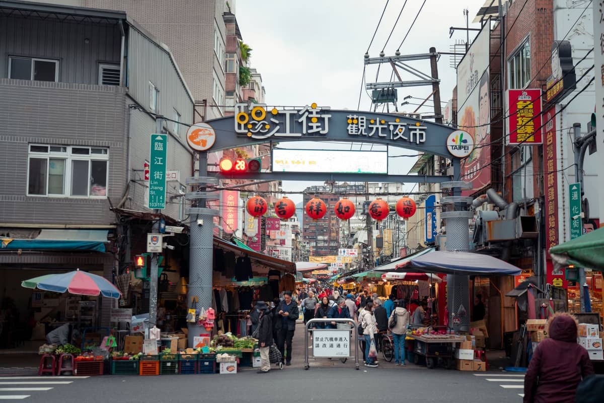 Eingang des Tonghua Nachtmarkts (Linjiang Street Night Market) in Taipei, mit dem Markttor, roten Laternen, Straßenständen und Besuchern, die in den belebten Nachtmarkt strömen.