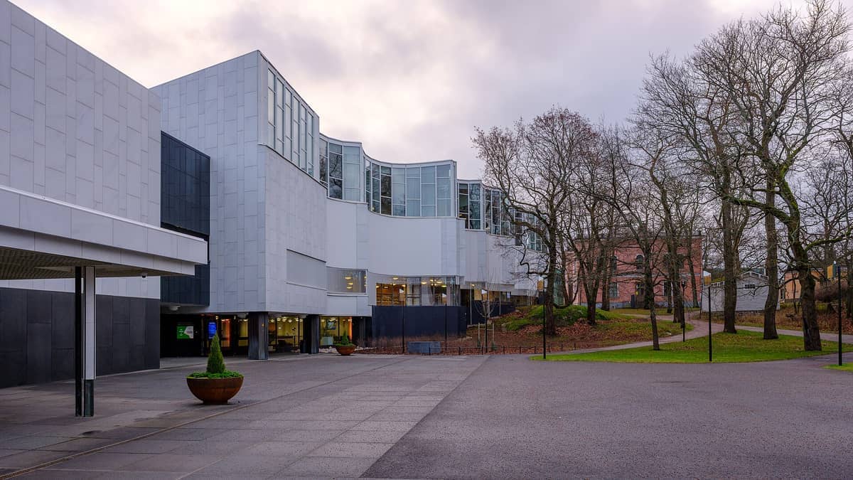 Fachada branca moderna do Museu Nacional de Arte Moderna da Finlândia em Töölö, Helsinque, com árvores sem folhas e céu nublado de inverno.