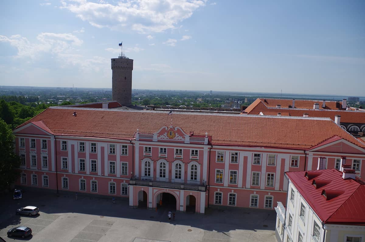 Weitläufiger Blick auf die markante rosa Barockfassade und den Turm der Burg Toompea, dem estnischen Parlamentsgebäude, von oben im hellen Sommerlicht fotografiert.