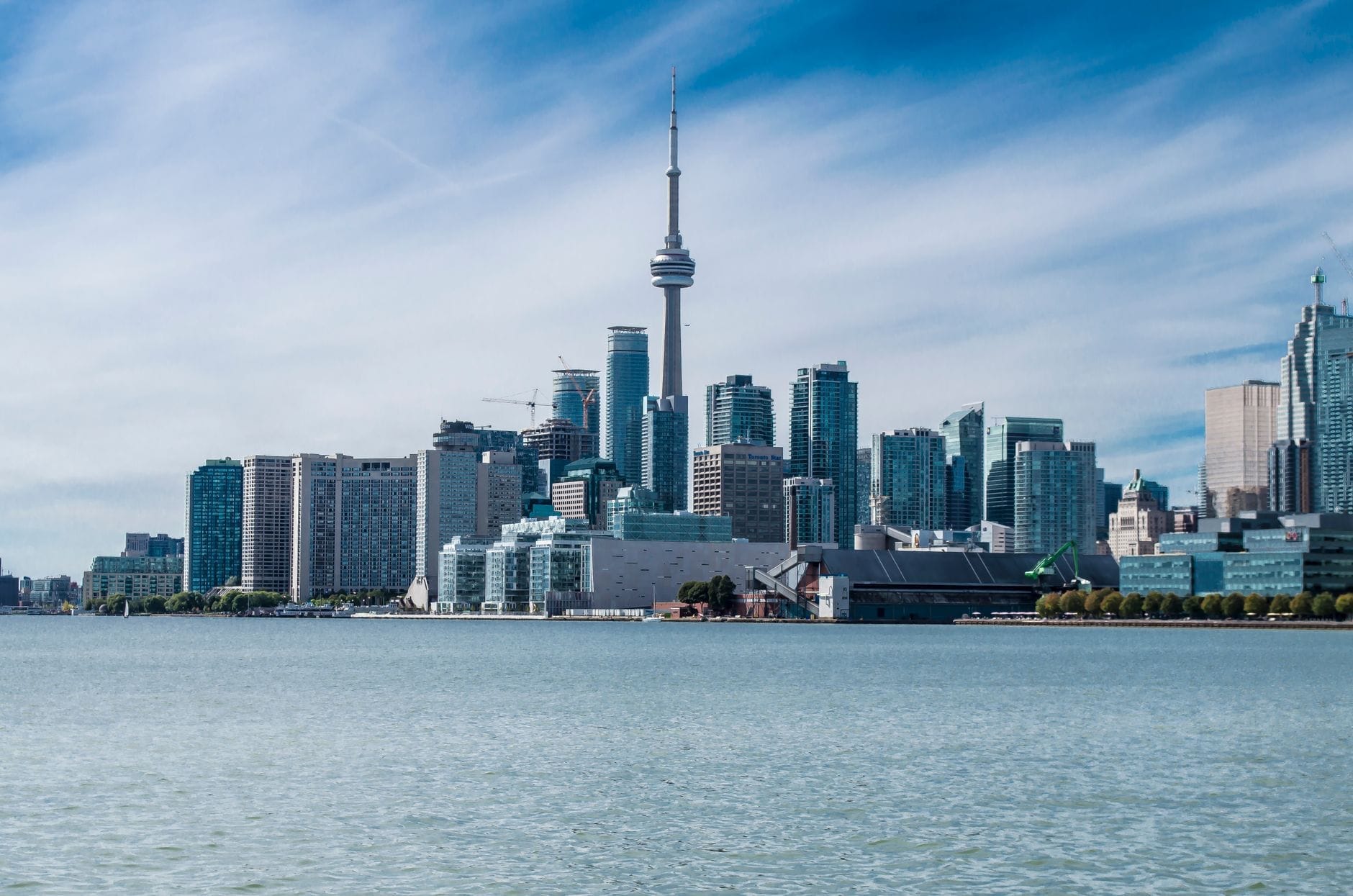 Horizonte de Toronto visto da orla marítima, com a CN Tower e os arranha-céus do centro sob um céu azul com nuvens tênues.