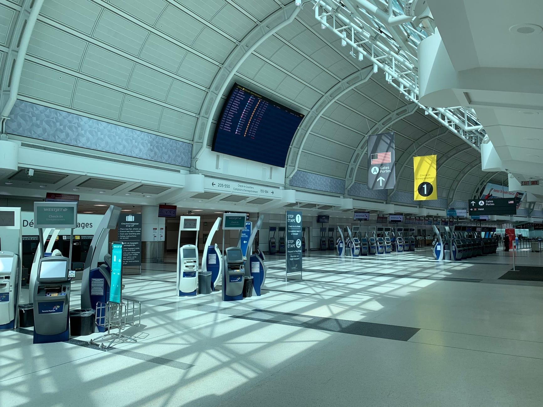 Terminal iluminado do aeroporto Toronto Pearson com quiosques de check-in automático, painéis de partidas e teto abobadado de vidro.