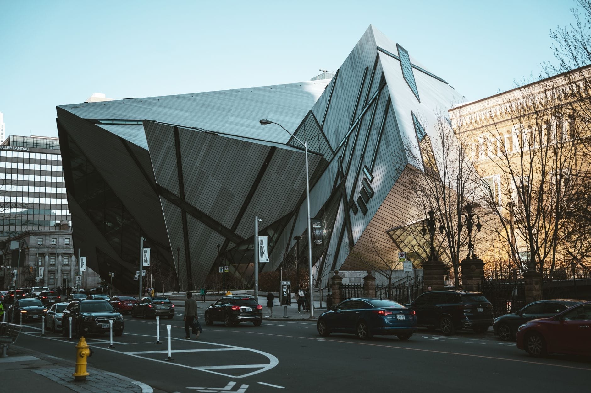 Vista da rua da icônica adição Crystal do Royal Ontario Museum de Toronto, com formas geométricas acentuadas e vidro, com carros e pessoas nas proximidades.