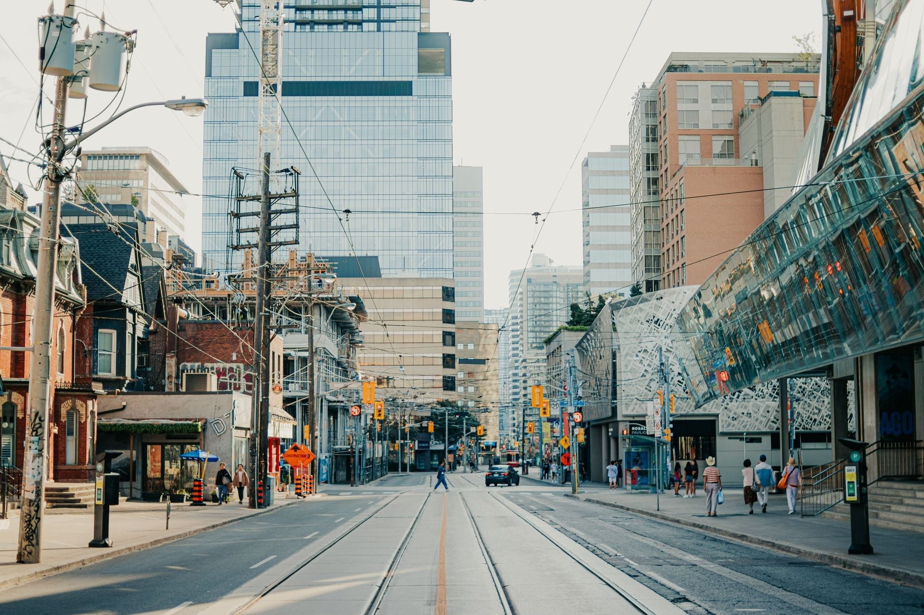 Uma rua ensolarada de Toronto com edifícios modernos, trilhos de bonde, pessoas caminhando e uma mistura arquitetônica no centro da cidade.