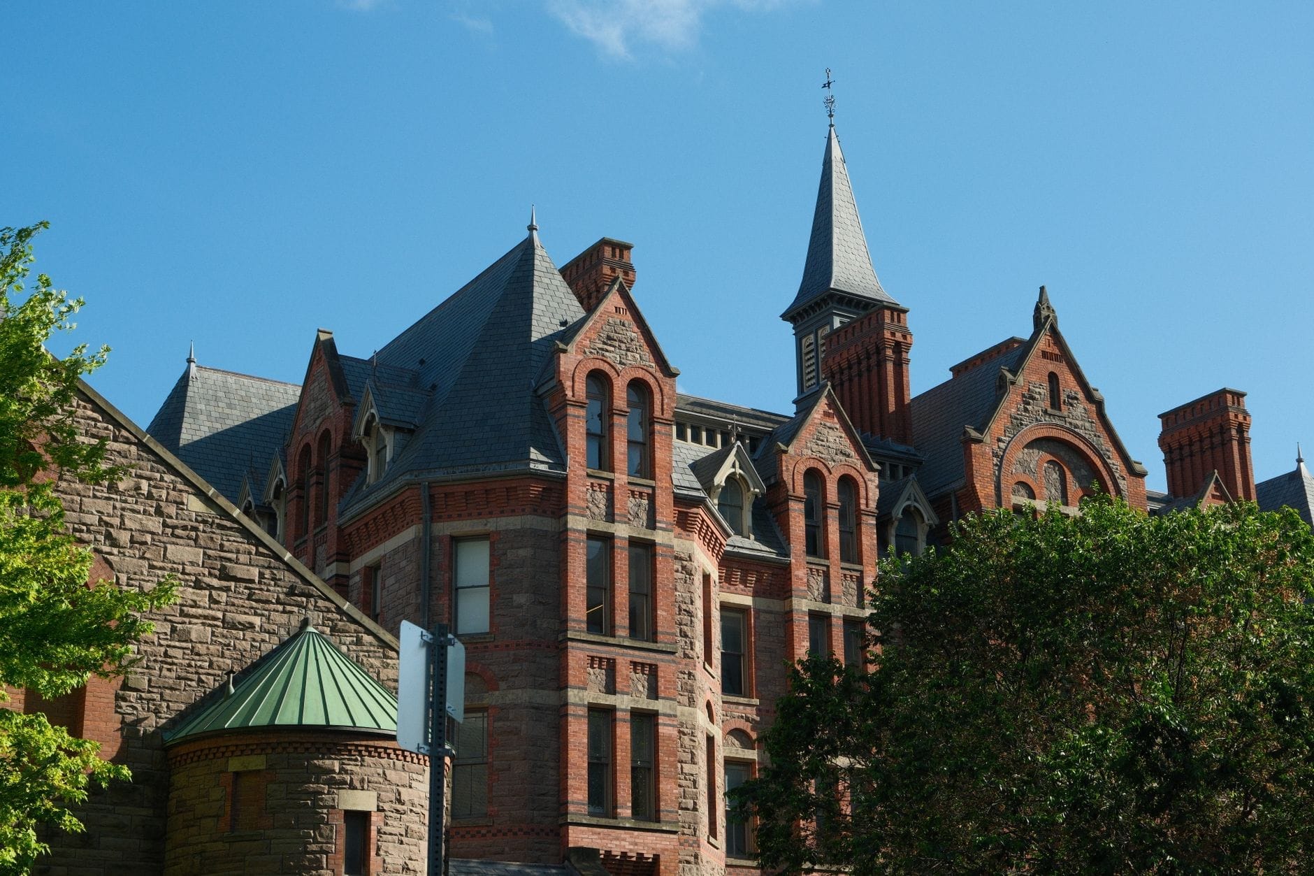 Edifício de tijolos vermelhos da era vitoriana com telhados pontiagudos e torres contra um céu azul e árvores em Toronto.