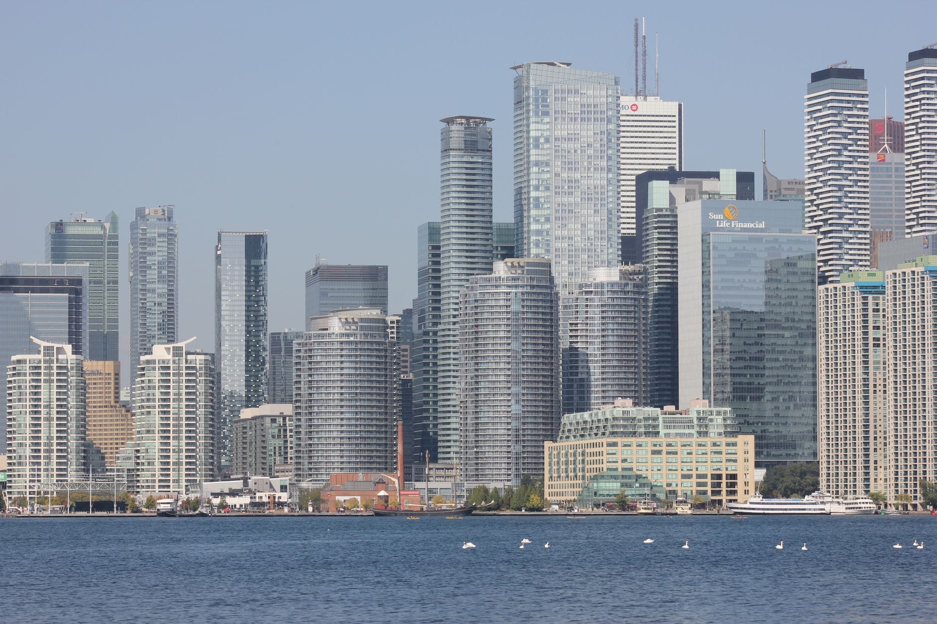 O horizonte do centro de Toronto com hotéis de grande altura à beira-mar, edifícios modernos e água azul cristalina sob um céu claro.