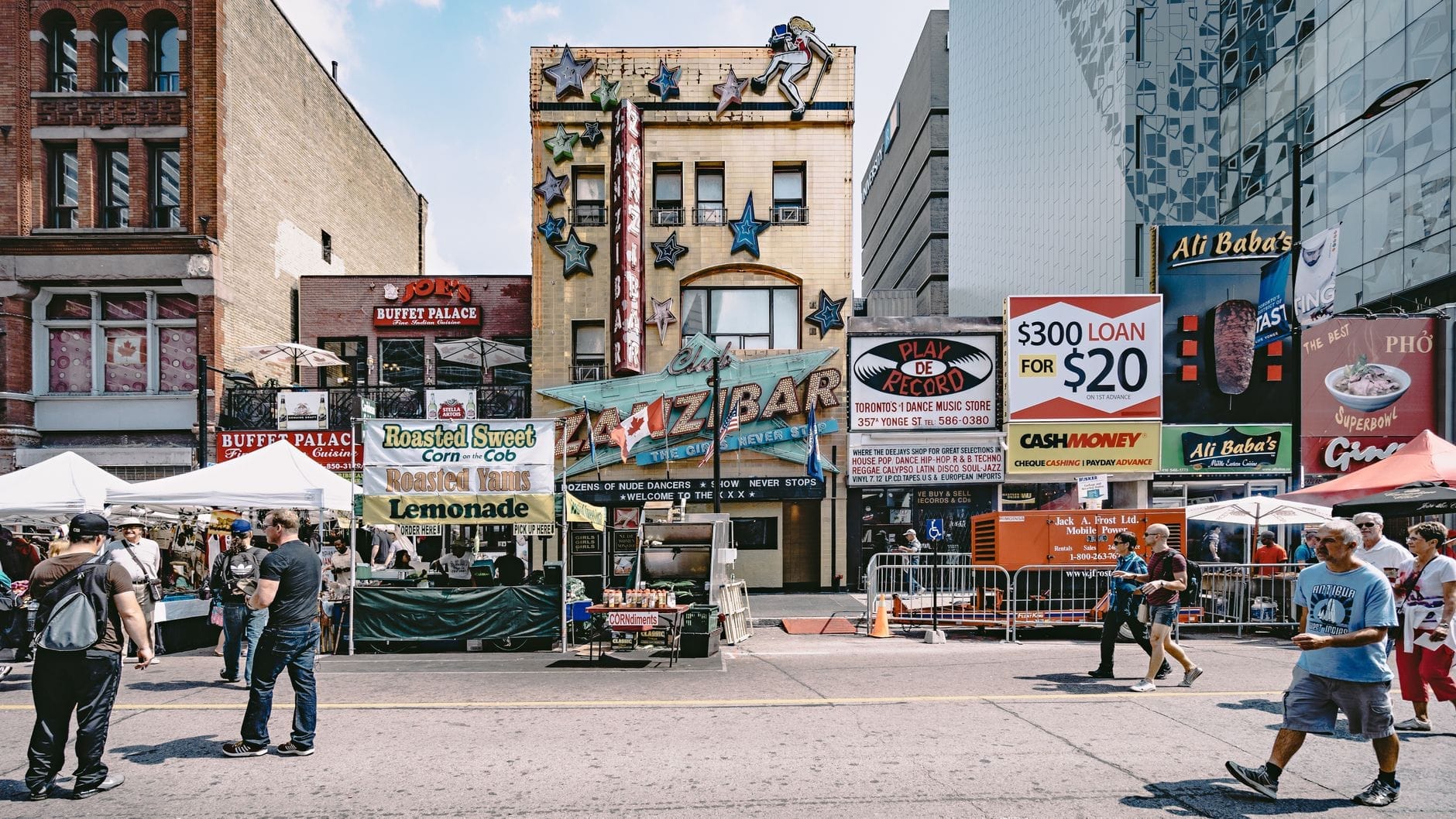 Movimentada rua de Toronto repleta de barracas de comida diversas e restaurantes, letreiros coloridos e pessoas caminhando, evocando a atmosfera vibrante de um corredor gastronômico.