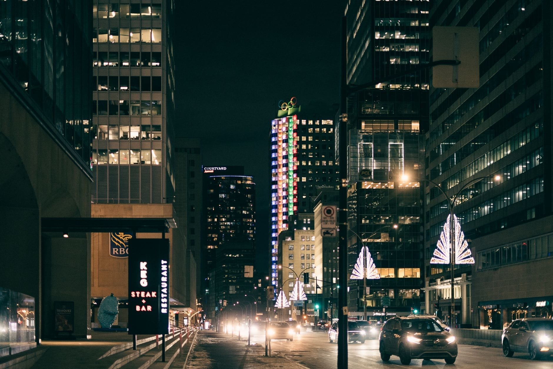 Vista noturna do centro de Toronto com arranha-céus iluminados, carros e uma placa do The Keg Steakhouse, sugerindo uma refeição sofisticada na cidade.