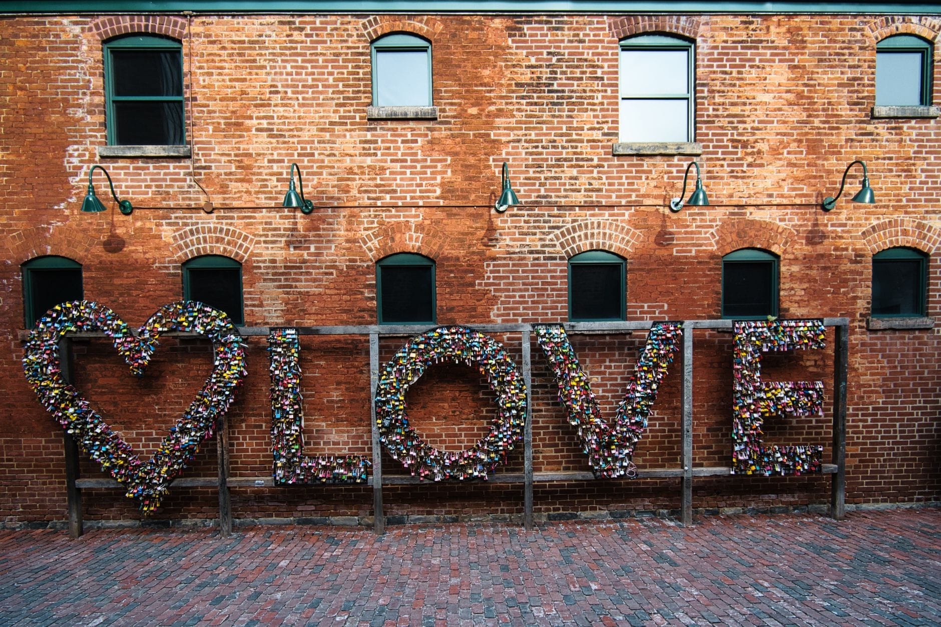 Grande letreiro LOVE coberto de cadeados contra uma parede de tijolos vermelhos e uma ruela de paralelepípedos no Distillery District de Toronto.