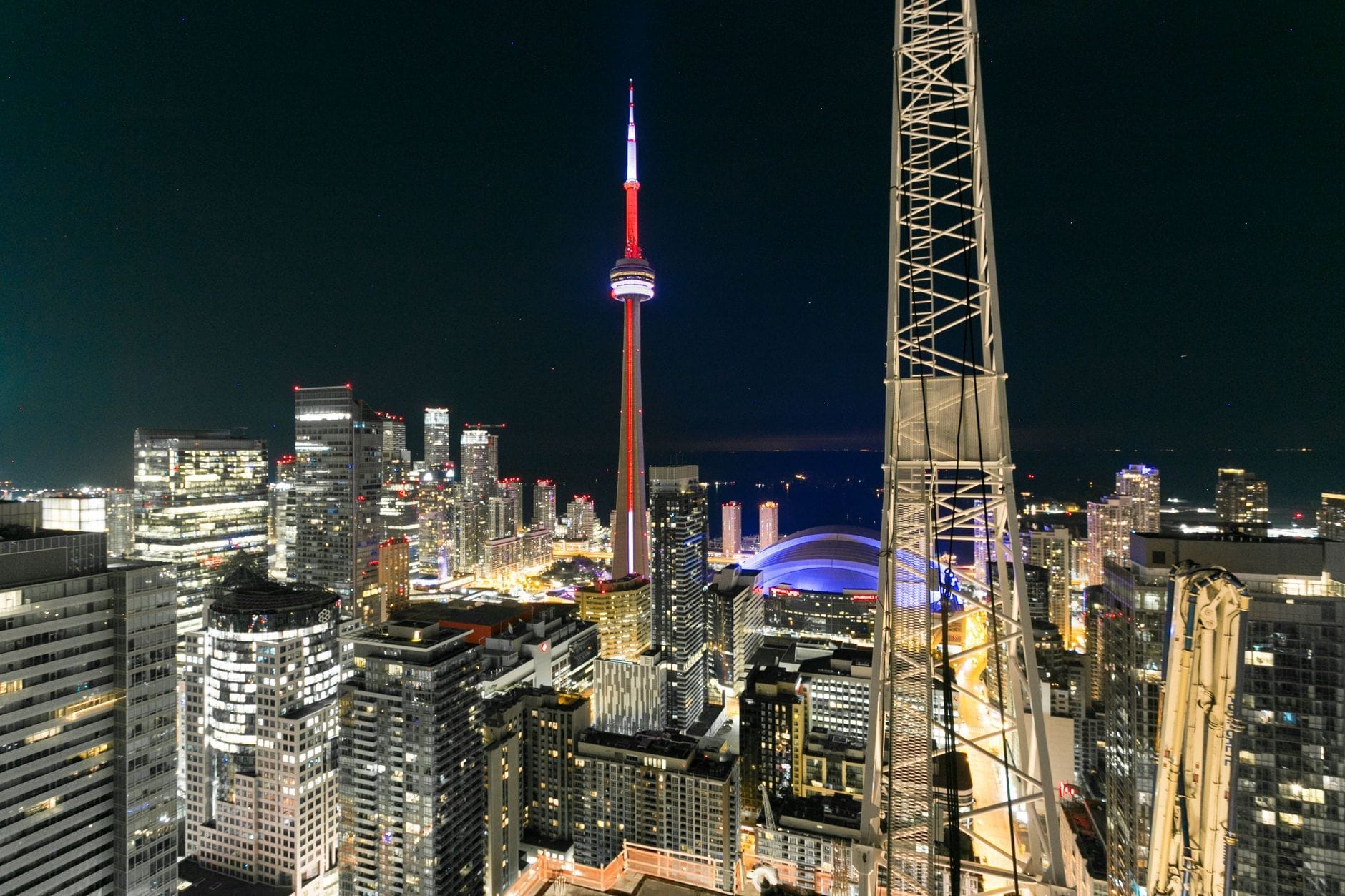 Vista noturna do horizonte de Toronto com a CN Tower visivelmente iluminada, cercada por arranha-céus e luzes da cidade, vista de um ponto elevado.