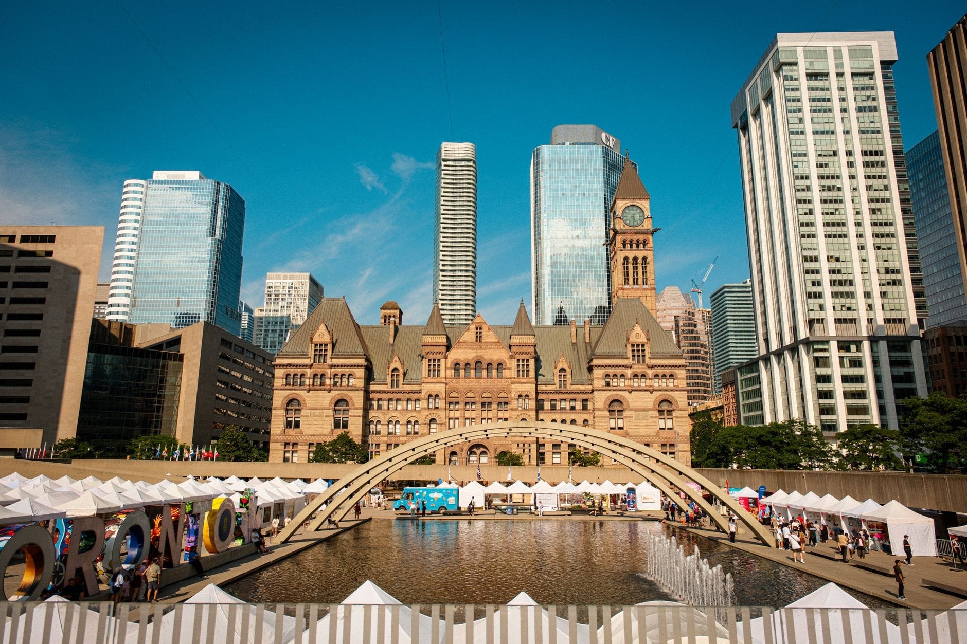 O Old City Hall de Toronto e os arranha-céus modernos dominam as tendas de um festival de verão e um espelho d'água em Nathan Phillips Square.