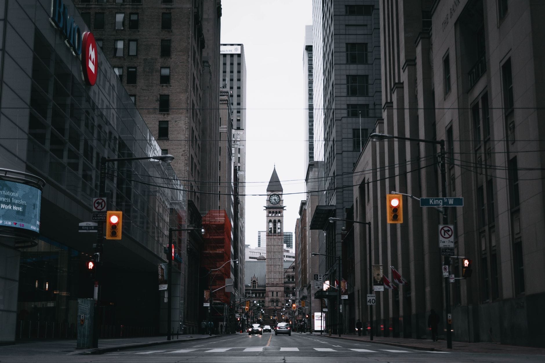 Vista da rua King Street West em Toronto com uma histórica torre do relógio ao fundo, rodeada de edifícios urbanos e sinalização de zona de festival.