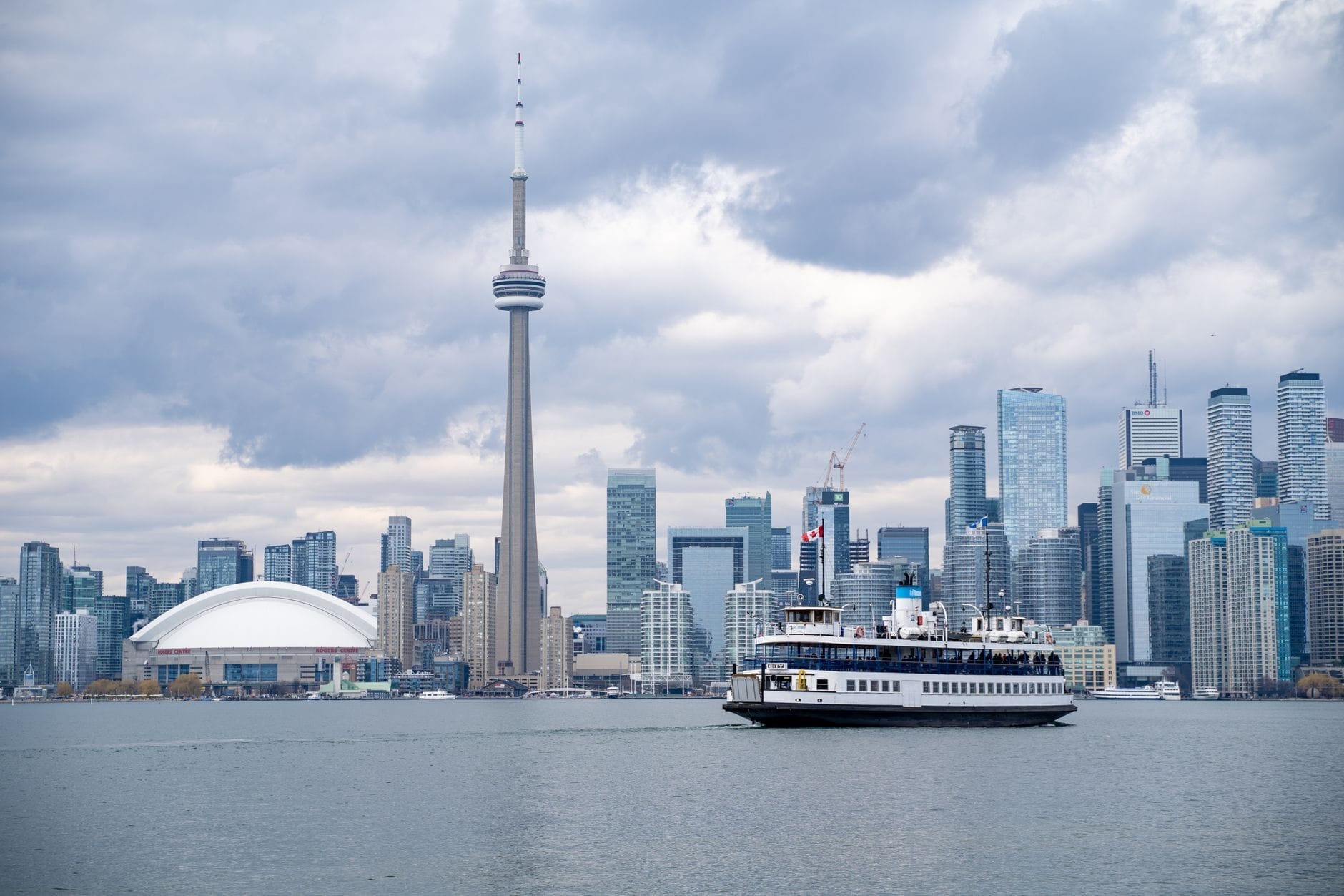 Balsa de Toronto atravessando a água com a CN Tower e o horizonte do centro da cidade ao fundo sob um céu nublado.